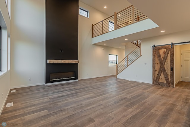 unfurnished living room with hardwood / wood-style flooring, a barn door, a high ceiling, and a fireplace