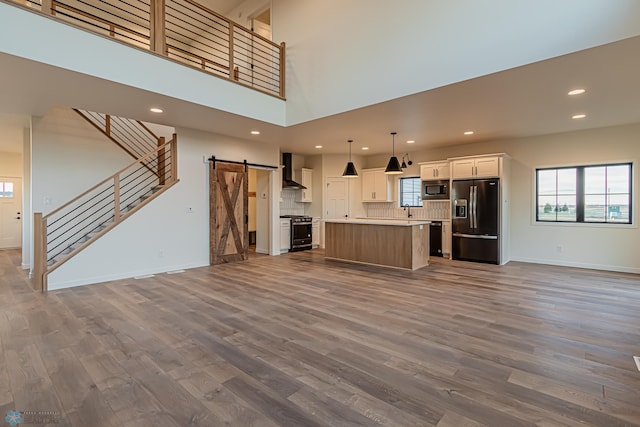 kitchen with wall chimney range hood, stainless steel microwave, a kitchen island, decorative light fixtures, and black refrigerator with ice dispenser