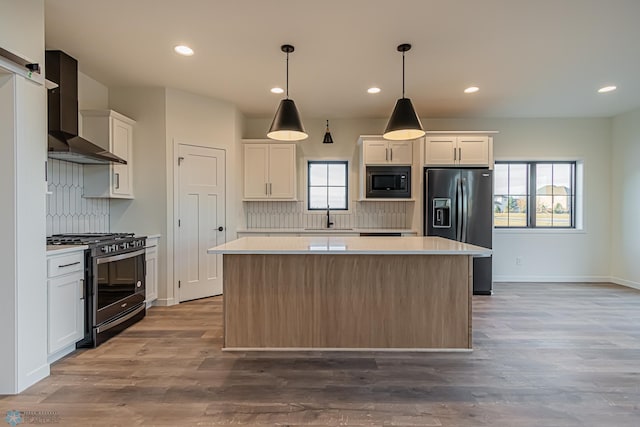 kitchen with white cabinetry, gas stove, black fridge, and wall chimney exhaust hood