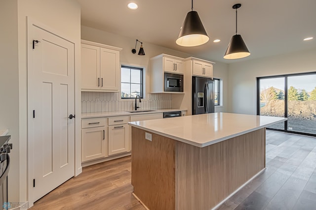 kitchen featuring decorative light fixtures, white cabinetry, sink, a center island, and black appliances