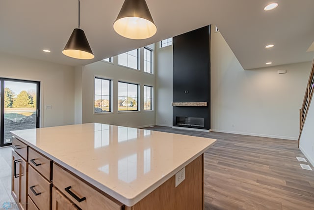 kitchen featuring hardwood / wood-style floors, light stone counters, a large fireplace, a kitchen island, and decorative light fixtures