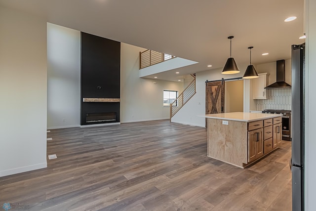 kitchen with stainless steel range oven, decorative light fixtures, a center island, a barn door, and wall chimney range hood