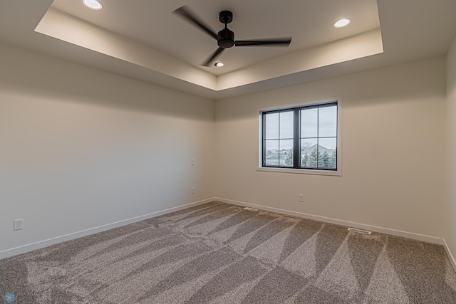 empty room with a tray ceiling, ceiling fan, and carpet flooring