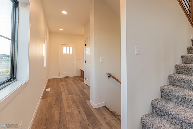 corridor featuring recessed lighting, baseboards, wood finished floors, and stairway