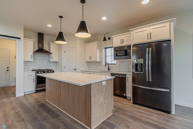 kitchen featuring wall chimney range hood, backsplash, a kitchen island, appliances with stainless steel finishes, and a sink