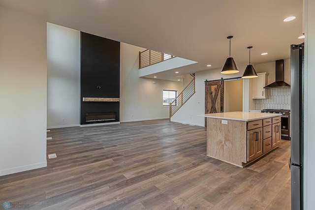 kitchen featuring a barn door, wall chimney exhaust hood, stainless steel appliances, baseboards, and dark wood-type flooring