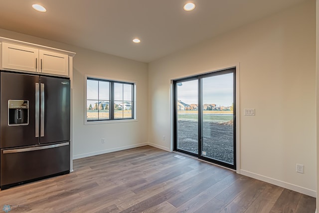 kitchen with baseboards, white cabinetry, refrigerator with ice dispenser, and light wood-style flooring