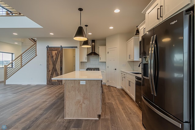 kitchen featuring a center island, a barn door, wall chimney exhaust hood, tasteful backsplash, and black fridge