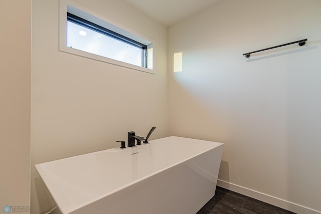 bathroom featuring baseboards, a freestanding bath, and wood finished floors