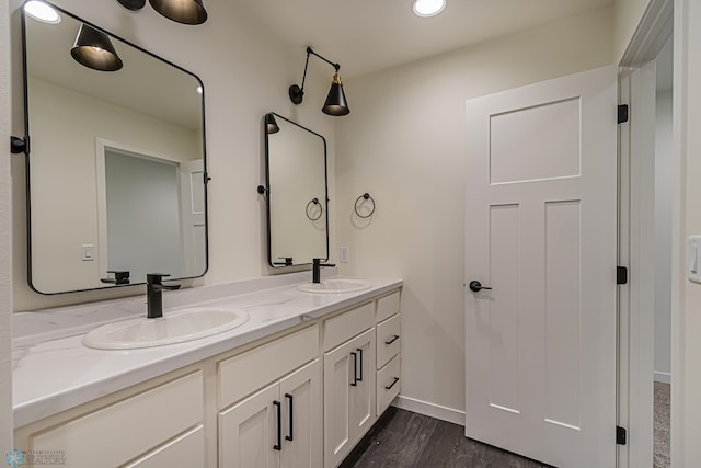 full bath with double vanity, baseboards, a sink, and wood finished floors