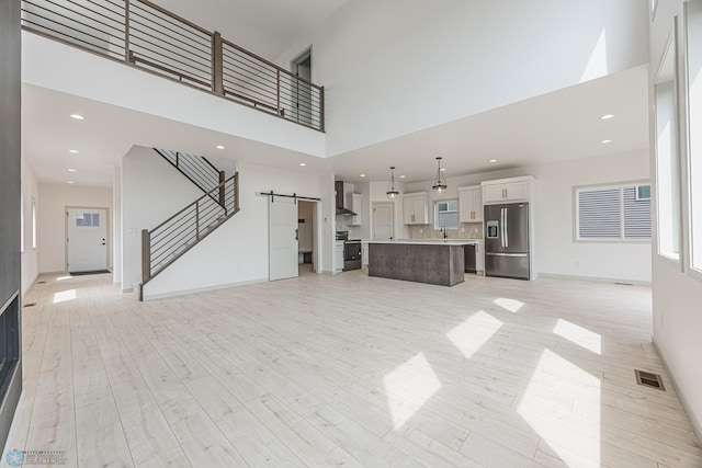 1264 Marlys Dr W, West Fargo, ND 58078 - unfurnished living room featuring a barn door, a towering ceiling, light wood-style flooring, stairs, and recessed lighting