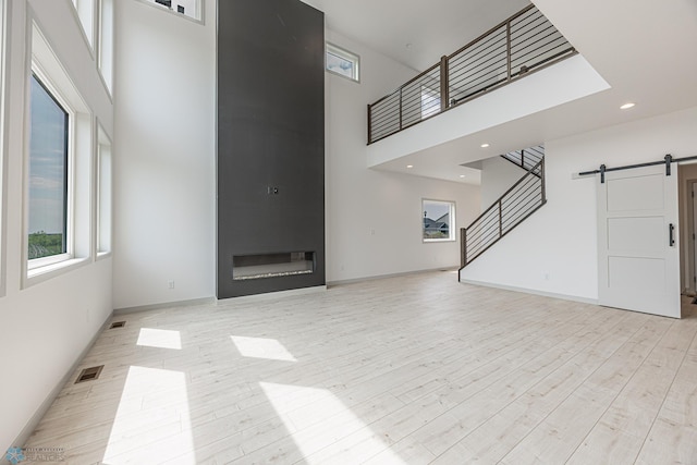 1264 Marlys Dr W, West Fargo, ND 58078 - unfurnished living room with a towering ceiling, a barn door, stairs, light wood-style flooring, and a large fireplace
