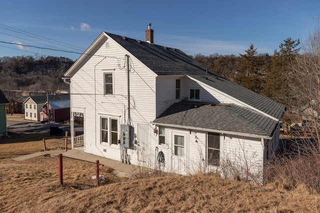 rear view of house with roof with shingles and a chimney