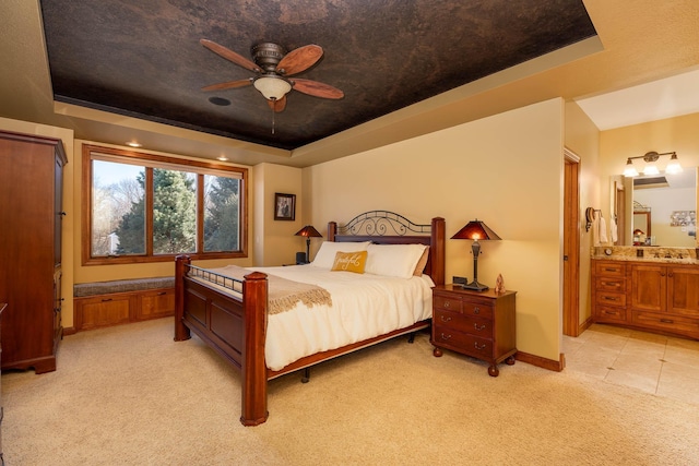 bedroom with light carpet, baseboards, a ceiling fan, ensuite bath, and a tray ceiling