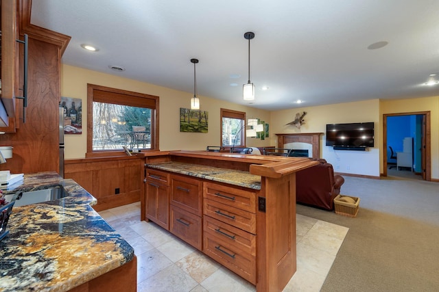 kitchen featuring decorative light fixtures, open floor plan, a kitchen island, a sink, and dark stone countertops