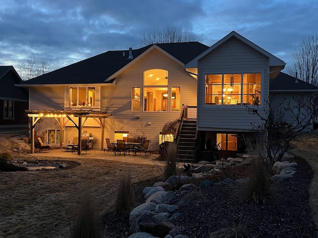 back of house at dusk featuring stairs and a patio