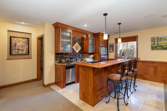 bar with pendant lighting, indoor wet bar, stainless steel appliances, backsplash, and wainscoting