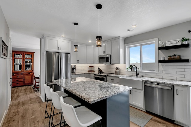 kitchen with sink, appliances with stainless steel finishes, a center island, light stone counters, and decorative light fixtures