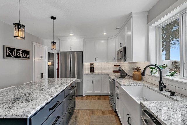 kitchen featuring white cabinetry, light stone counters, decorative light fixtures, and appliances with stainless steel finishes