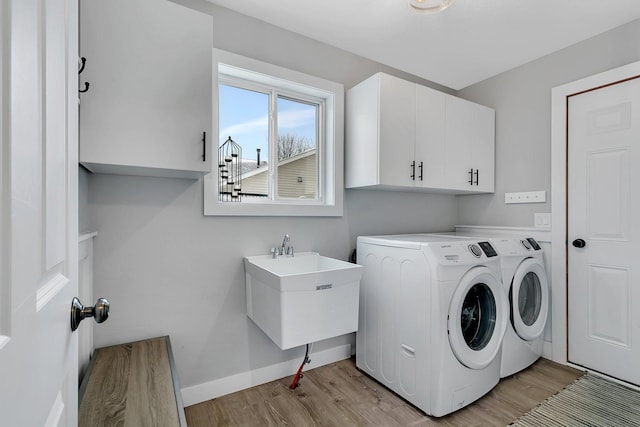 laundry room featuring cabinets, sink, washing machine and clothes dryer, and light hardwood / wood-style flooring