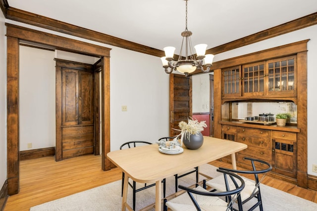 dining space with a notable chandelier, light wood finished floors, baseboards, and crown molding