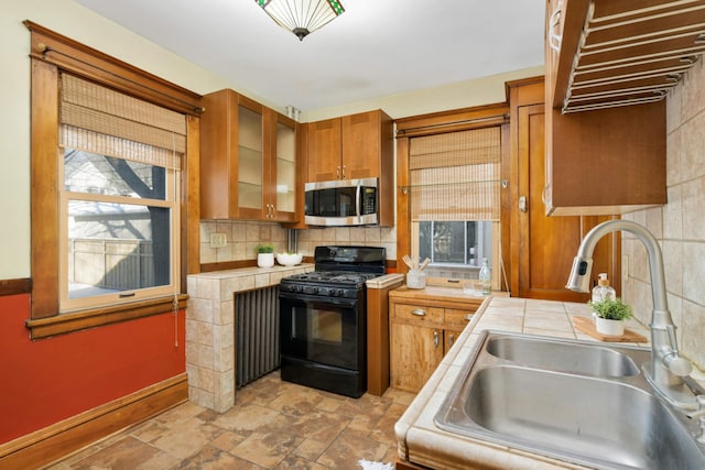 kitchen featuring stainless steel microwave, glass insert cabinets, brown cabinetry, black range with gas cooktop, and a sink