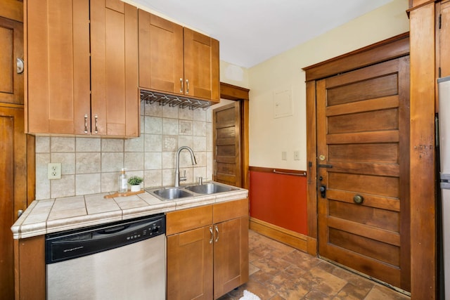 kitchen featuring tile counters, brown cabinetry, dishwasher, backsplash, and a sink