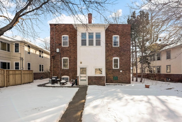 snow covered back of property with brick siding, a chimney, and stucco siding