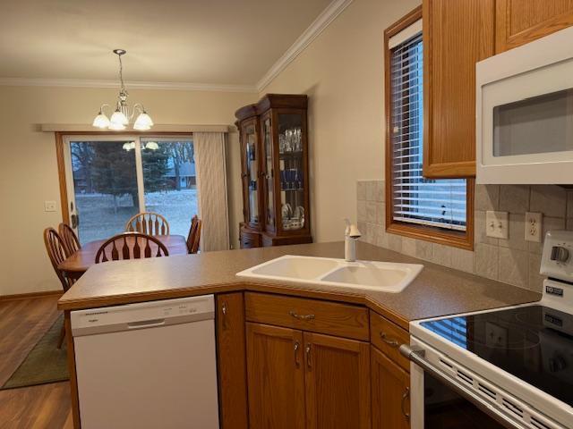 kitchen with sink, crown molding, a notable chandelier, white appliances, and decorative backsplash