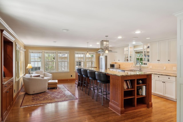 kitchen featuring a breakfast bar area, hanging light fixtures, stainless steel refrigerator, a kitchen island, and white cabinets