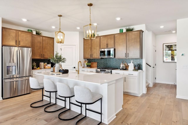 kitchen with sink, decorative light fixtures, light hardwood / wood-style flooring, an island with sink, and stainless steel appliances