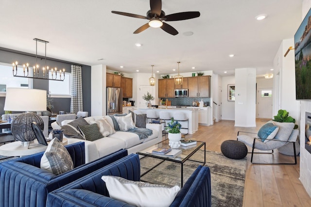 living room featuring ceiling fan with notable chandelier and light hardwood / wood-style floors