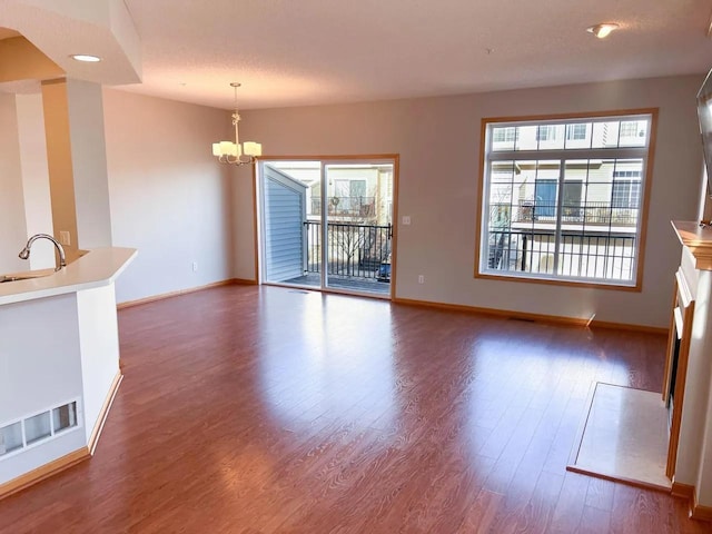 unfurnished living room featuring dark wood-type flooring, plenty of natural light, a textured ceiling, and a notable chandelier