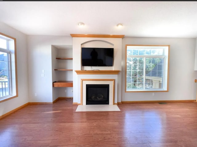 unfurnished living room featuring a wealth of natural light, baseboards, wood finished floors, and a fireplace with flush hearth