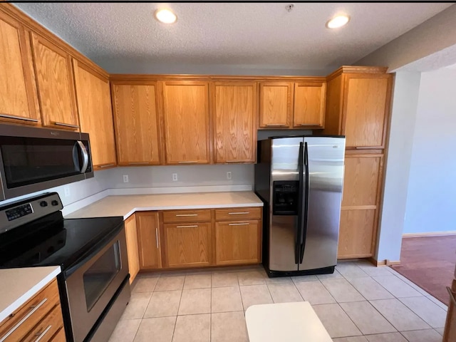 kitchen with light tile patterned floors, stainless steel appliances, brown cabinets, and light countertops