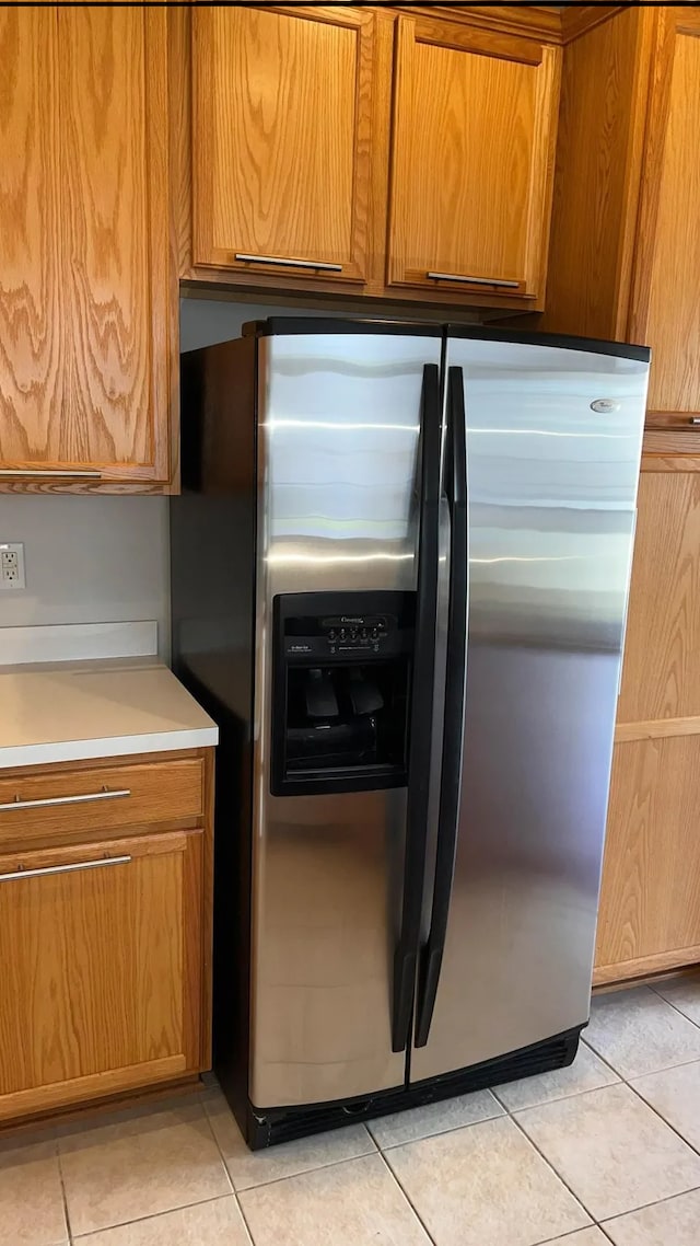 kitchen featuring brown cabinetry, light tile patterned flooring, stainless steel fridge with ice dispenser, and light countertops