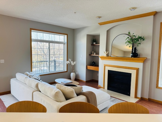 living area with a fireplace with flush hearth, built in features, a textured ceiling, wood finished floors, and baseboards