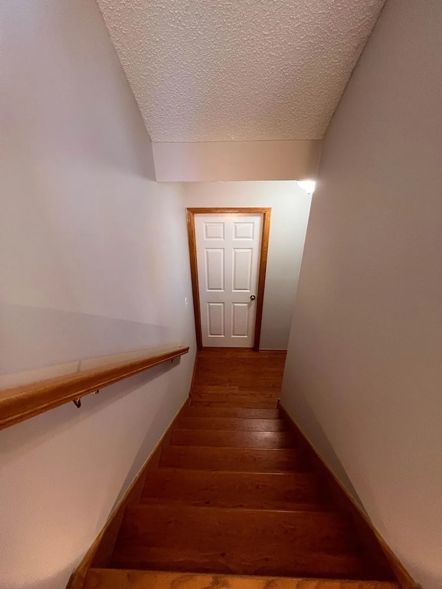 staircase featuring a textured ceiling, baseboards, and hardwood / wood-style flooring