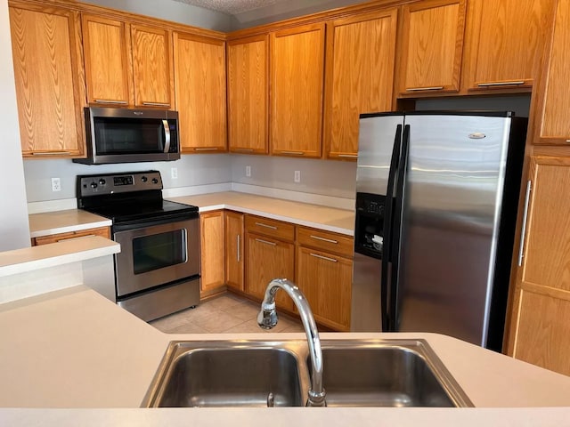 kitchen with a sink, appliances with stainless steel finishes, light tile patterned floors, and light countertops