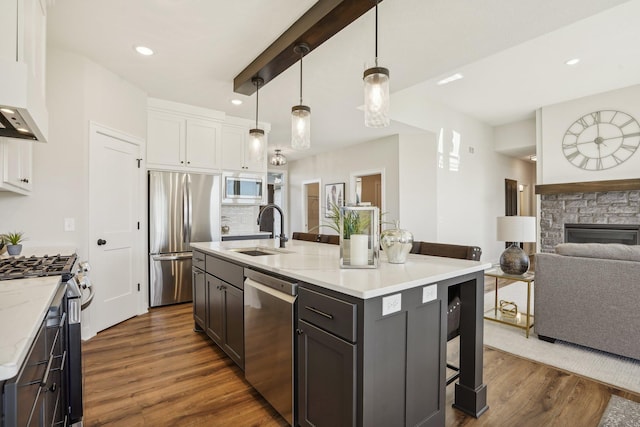 kitchen with sink, appliances with stainless steel finishes, white cabinetry, a kitchen island with sink, and decorative light fixtures