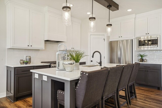 kitchen with an island with sink, sink, white cabinets, hanging light fixtures, and stainless steel appliances