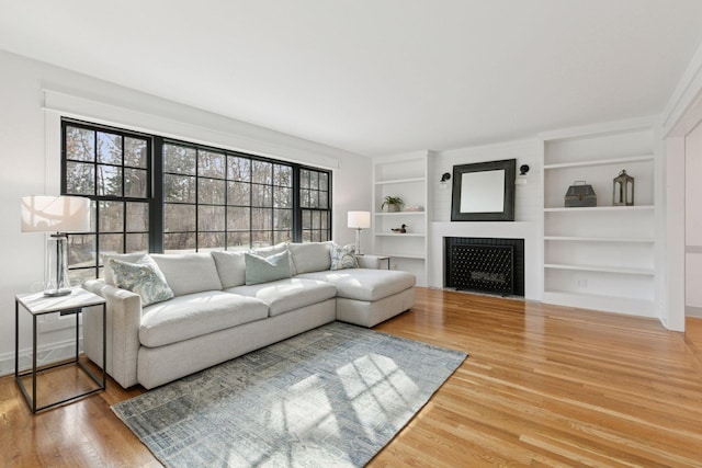 living room with baseboards, a fireplace with flush hearth, built in features, and wood finished floors