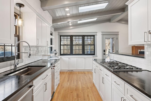 kitchen featuring vaulted ceiling with skylight, white cabinetry, stainless steel appliances, and a sink