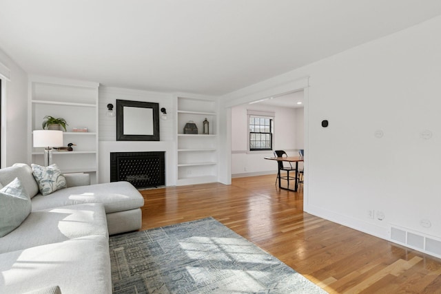 living area featuring built in shelves, a fireplace, visible vents, wood finished floors, and baseboards