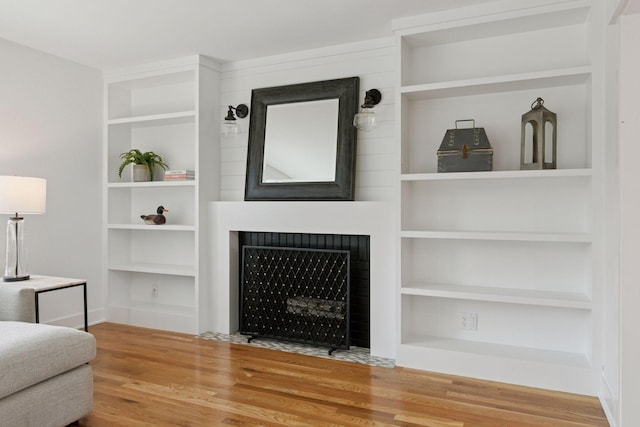 living area featuring a fireplace with flush hearth, built in shelves, and wood finished floors