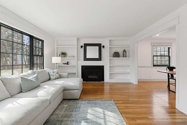 living area featuring a fireplace with flush hearth, built in features, baseboards, and light wood finished floors