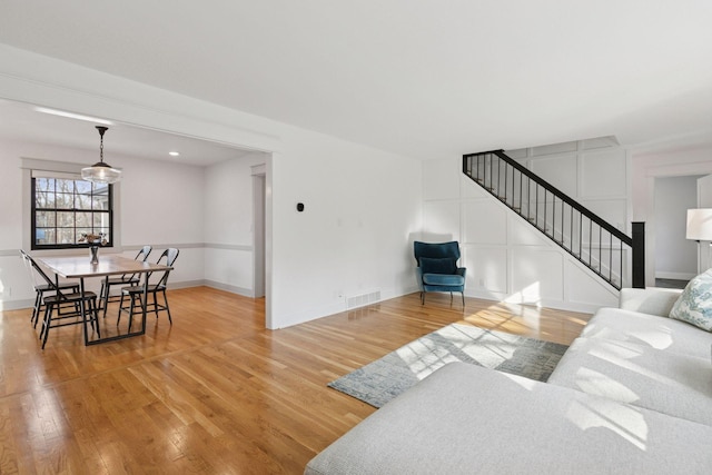 living area featuring visible vents, a decorative wall, wood finished floors, baseboards, and stairs