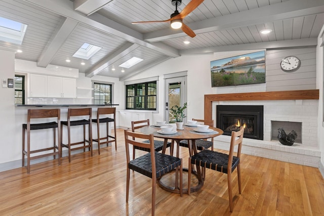 dining room with a ceiling fan, lofted ceiling with skylight, light wood-style flooring, a fireplace, and recessed lighting