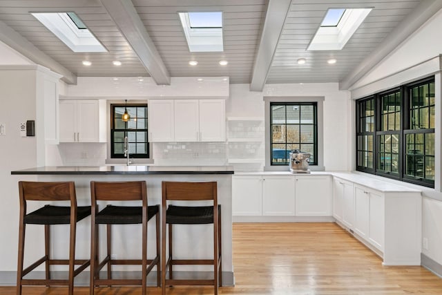 kitchen featuring tasteful backsplash, white cabinets, a breakfast bar area, a peninsula, and light wood-style floors