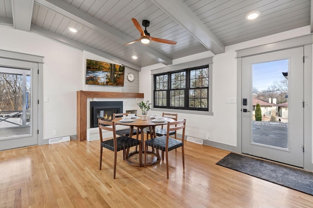 dining area featuring vaulted ceiling with beams, light wood-style flooring, a glass covered fireplace, and visible vents